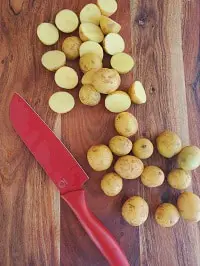 halved baby gold potatoes on a wooden board along with a red knife