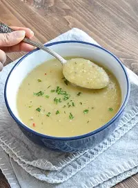 dairy free potato leek soup in a blue bowl with a spoon & garnished with parsley