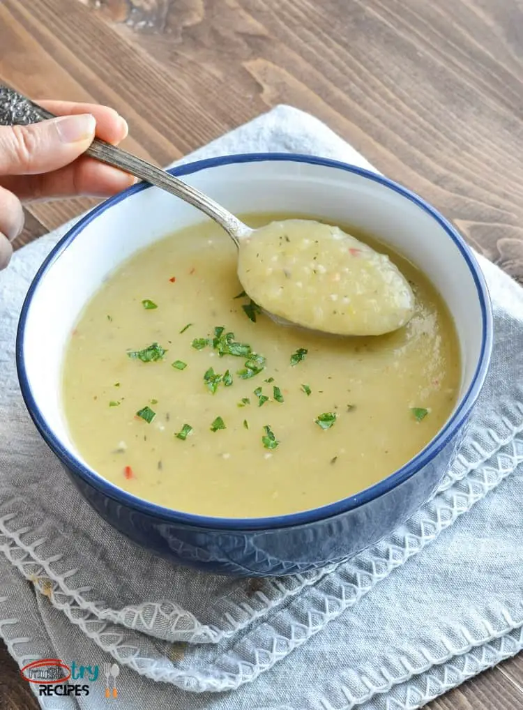 potato leek soup instant pot dairy free in a blue bowl on top of a grey linen & soup being lifted with a spoon