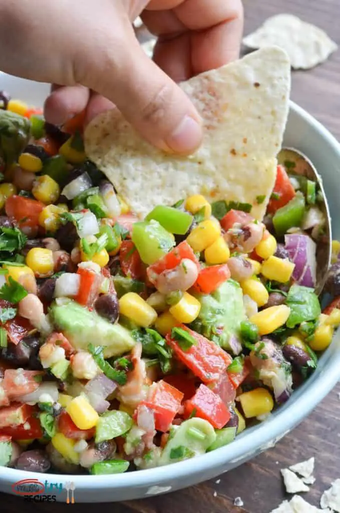 easy cowboy caviar dip in a light blue bowl and being lifted with a tortilla chip