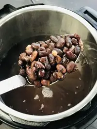 pressure cooked black beans in a ladle