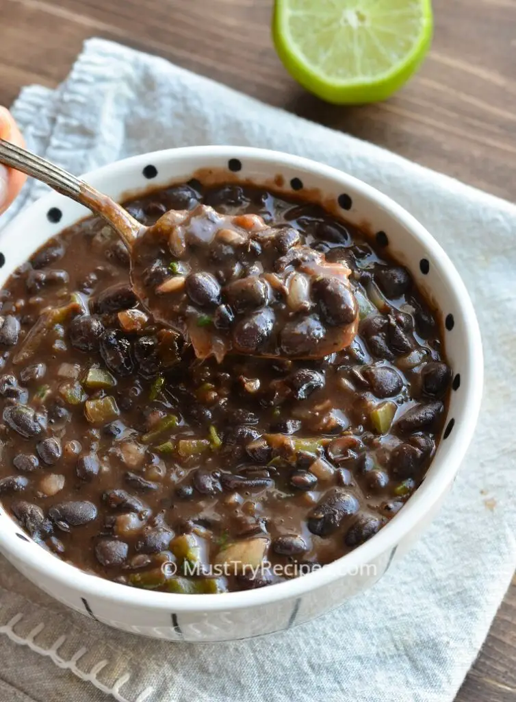 instant pot Cuban black beans served in a white bowl and beans being lifted with a spoon