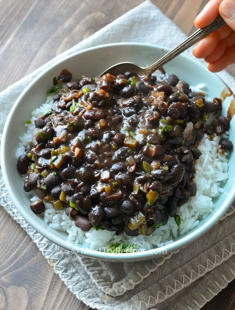 Instant pot Cuban style black beans served over white rice in a light blue bowl with a spoon