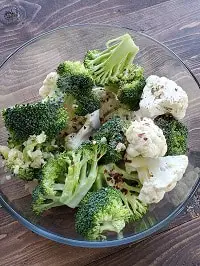 seasoning broccoli and cauliflower florets in a clear glass bowl