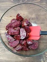 tossing beets in a clear bowl with a red spatula