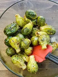 tossing brussel sprouts in a clear bowl with a red spatula