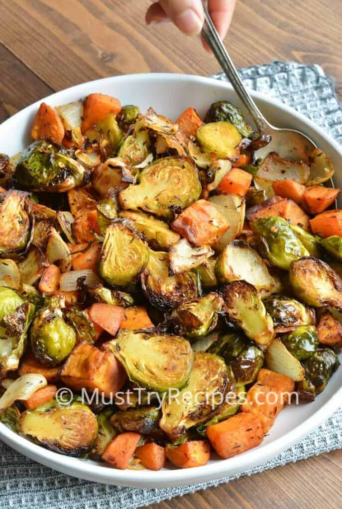 air fryer brussel sprouts and sweet potatoes in a white plate being lifted with a spoon