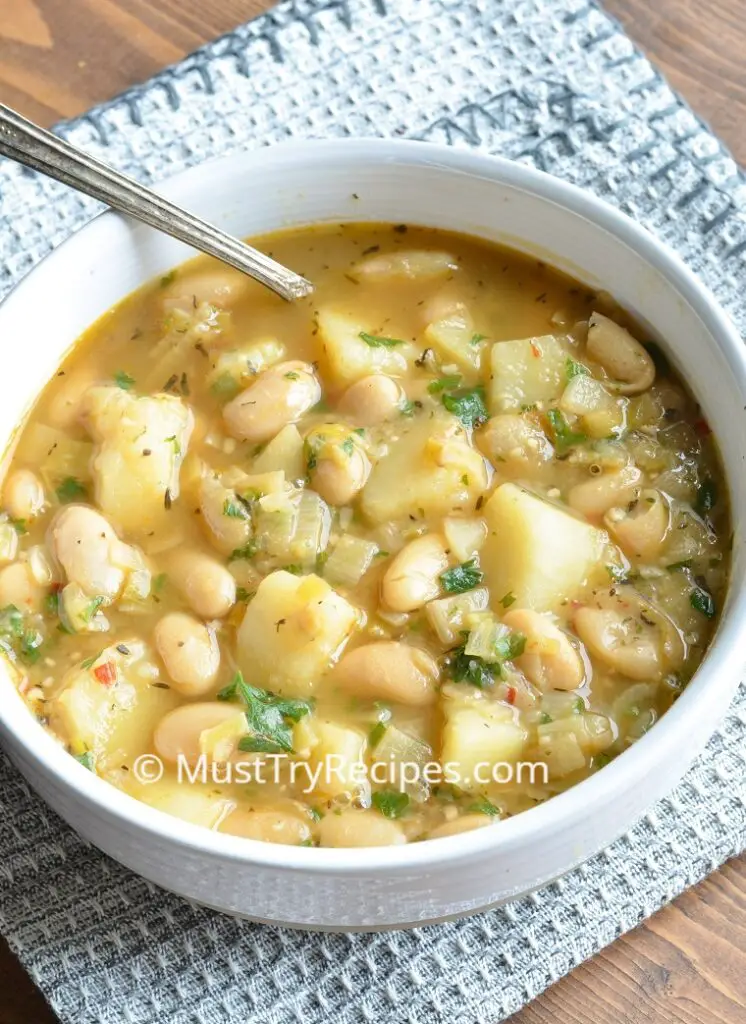 vegetarian bean and potato soup in a white bowl with a spoon