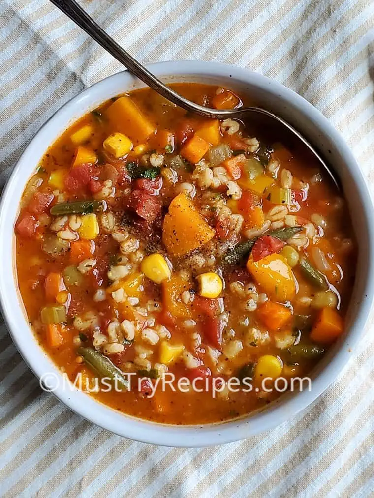 old fashioned vegetable barley soup in a white bowl with a spoon