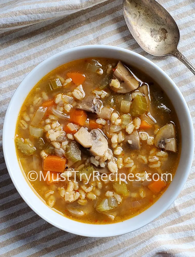 vegan mushroom barley soup in a white bowl with a spoon on the side