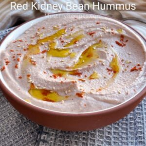 red kidney bean hummus in a terracota colored bowl with drizzles of olive oil. sesame seeds & paprika