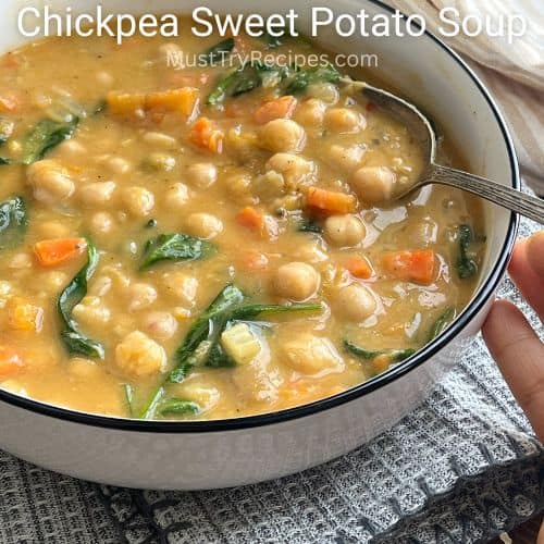 creamy chickpea sweet potato soup in a black rimmed white bowl with a silver spoon