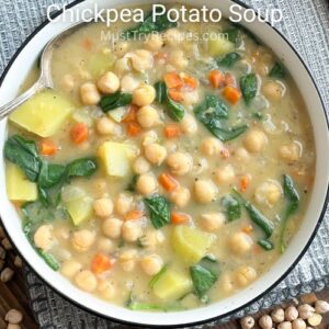 chickpea and potato soup in a black rimmed white bowl with a silver spoon