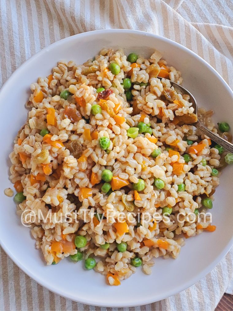 barley pilaf in a white plate with a silver spoon