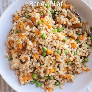 barley pilaf served in a white plate with a silver spoon.